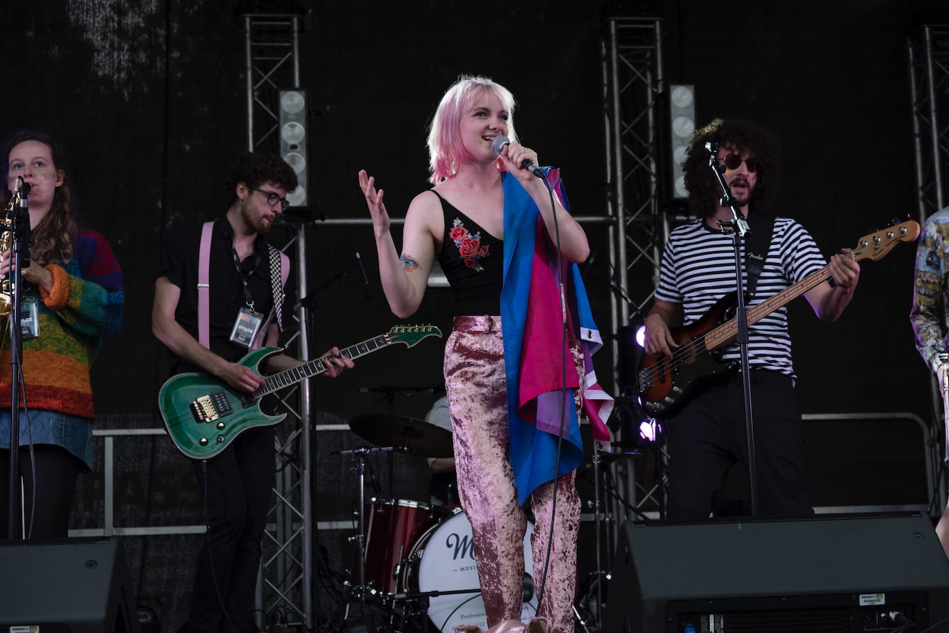 Our singer, Jazz, sings on stage at Cambridge Pride while draped in a flag representing bisexuality